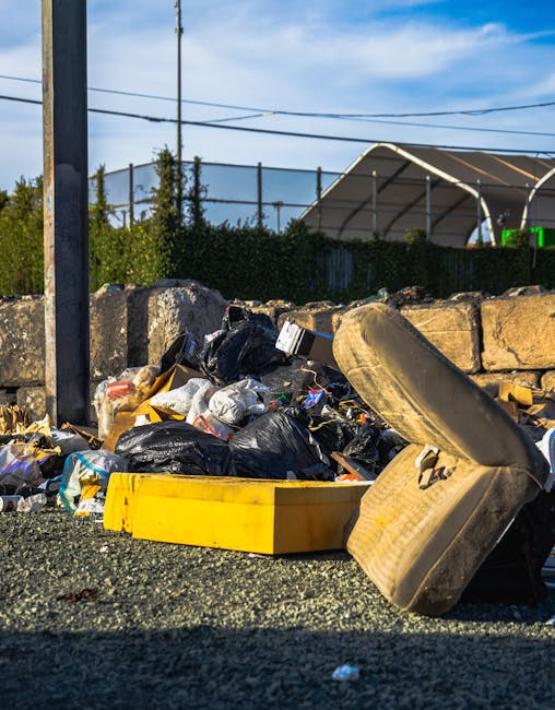 Three black plastic rubbish bags, partially crumpled and tied at the top, rest on the pavement in front of a black metal fence. The bags appear to contain waste materials and are positioned beside a c